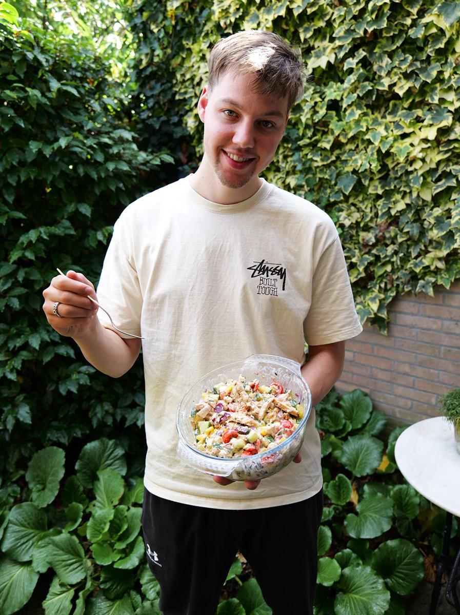 De coach staat buiten met een bakje gezond eten.